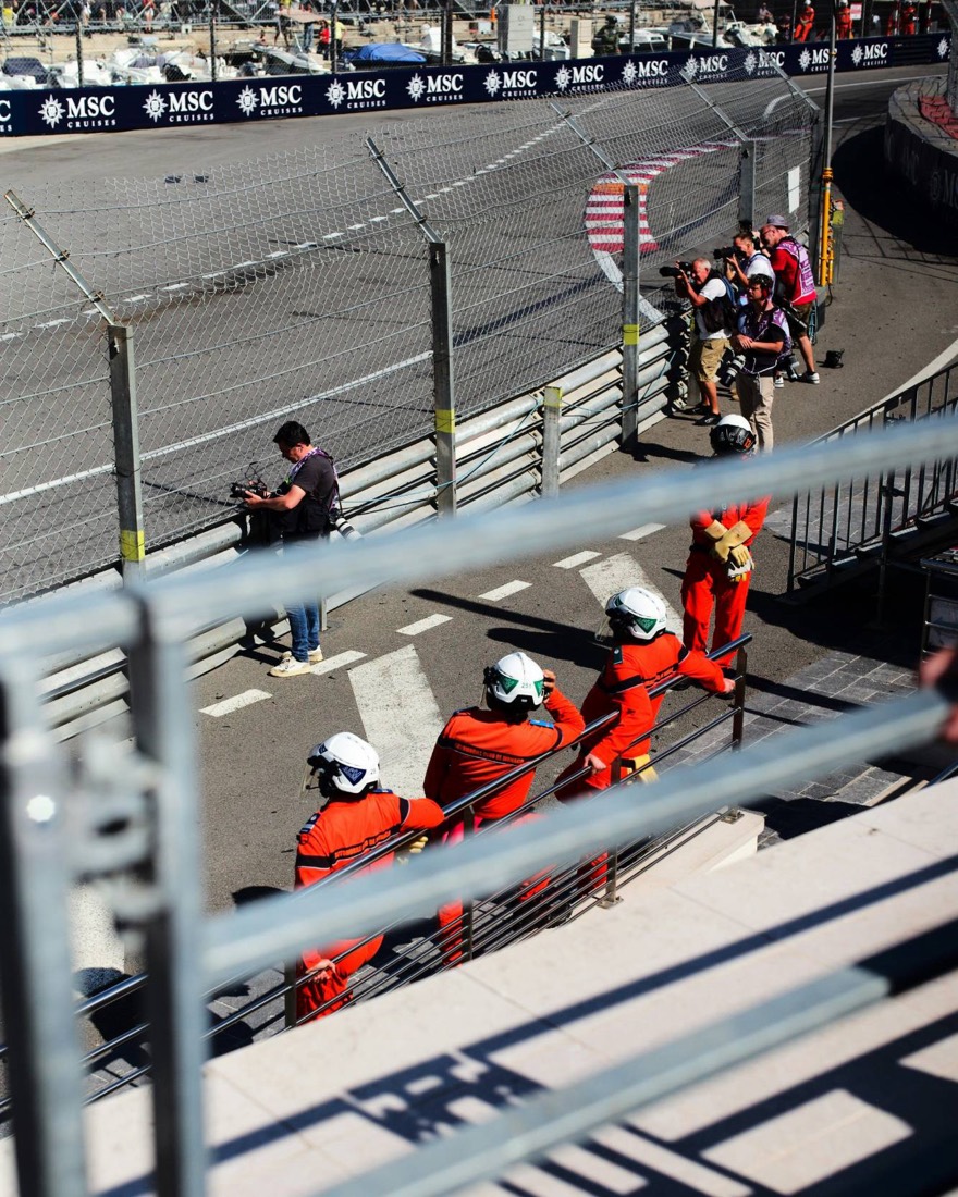 Comisarios con monos naranjas junto a la barrera durante el Gran Premio de Mónaco, con fotógrafos a lo largo de la pista