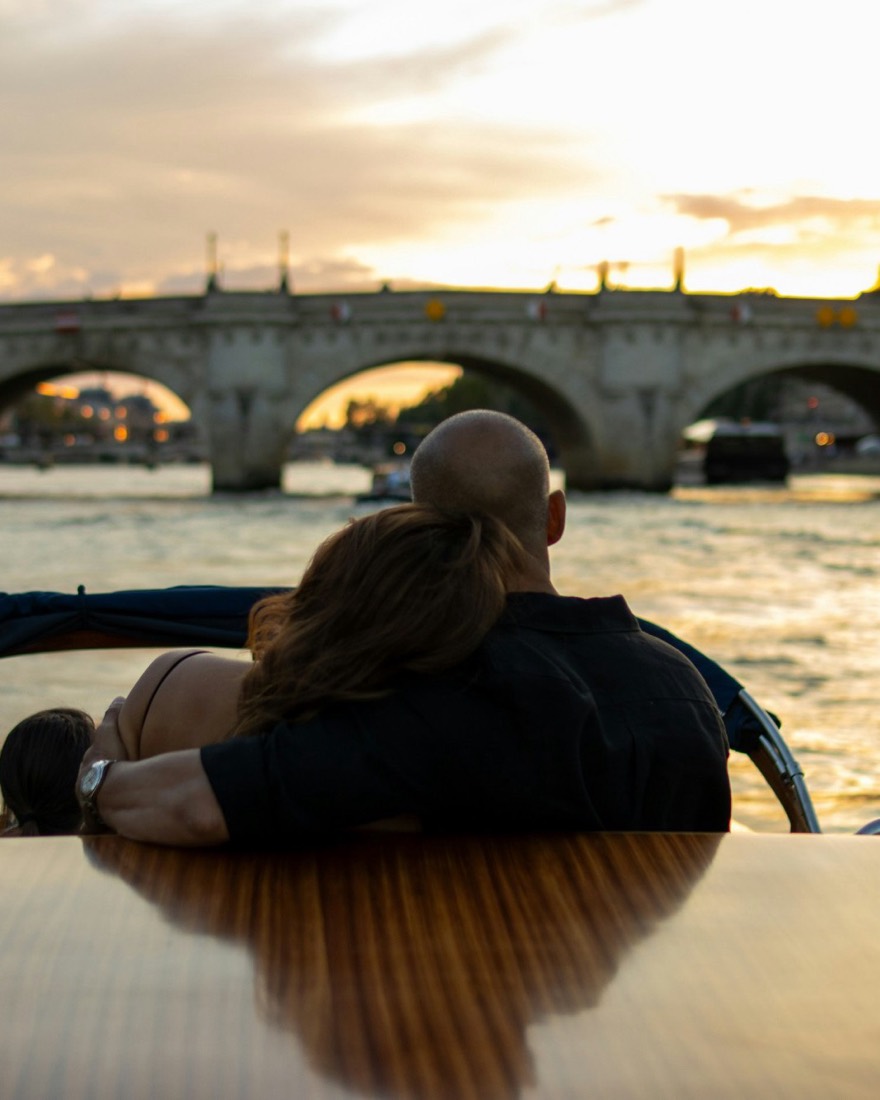 Invitados en el asiento trasero de una lancha de madera barnizada, rumbo al Pont Neuf al atardecer